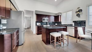 A modern kitchen with dark wood cabinets, a central island with stools, a microwave, and a sink.