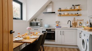 A modern kitchen with white cabinetry, a built-in oven, a microwave, and a washing machine. - Stables Cottage, Nethybeodge (Nethybridge)