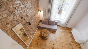 A room with a brick wall, wooden flooring, a mirrored wall, a cushioned seating area, and a round wooden stool. - Wilson Park Loft Studio with Mezzanine (Poznań)