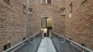 A narrow brick corridor with metal railings and a central staircase leading to an upper level. - Wilson Park Loft Studio with Mezzanine (Poznań)
