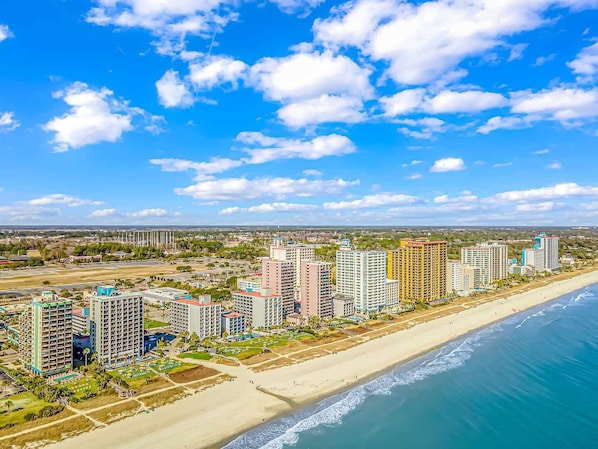 A coastal cityscape with high-rise buildings, a beach, and a clear sky.