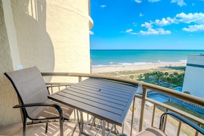 A balcony with a table and chair, overlooking a beach and ocean.
