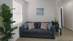 A living room with a grey sofa, a painting on the wall, and a large plant.