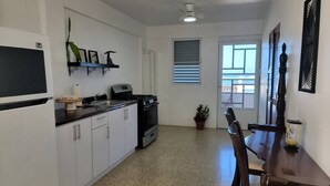 A compact kitchen with white cabinets, a black stove, and a dining area with a wooden table and chairs.