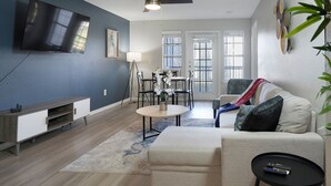 A modern living room with a flat-screen TV, a ceiling fan, a dining area with a table and chairs, and a sofa with a throw blanket. - Charming 2-bedroom apartment with WiFi, AC in pleasant Austin (Austin)