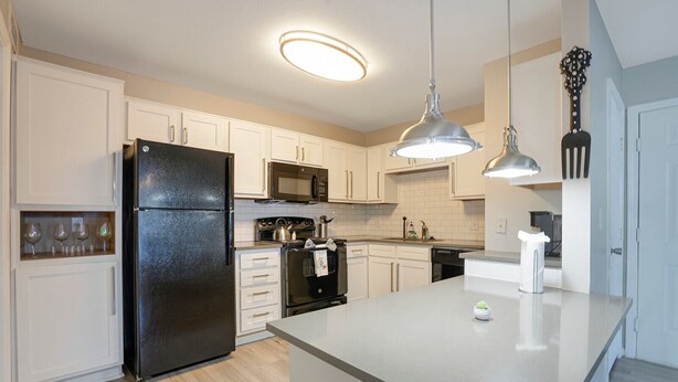 A modern kitchen with white cabinetry, a black refrigerator, a microwave, an oven, and a sink. There are two pendant lights above the island. - Charming 2-bedroom apartment with WiFi, AC in pleasant Austin (Austin)