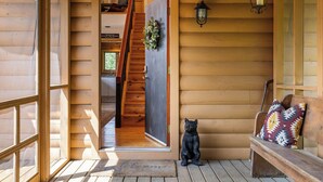 A wooden cabin entrance with a bench, a bear statue, a staircase, and a lantern. - Stunning Views Hilltop Cabin Near Homestead Resort! (Hot Springs)