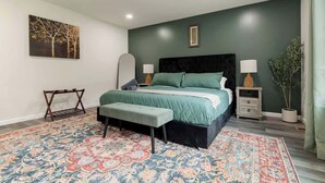 Ein Schlafzimmer mit Bett, Nachttischen, einer Bank, einem Teppich und einem Bild an der Wand.