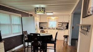 A dining area with a wooden table and chairs, a kitchen in the background, and a hallway leading to another room.