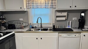 A kitchen with white cabinets, a stainless steel sink, a coffee maker, and a dishwasher.