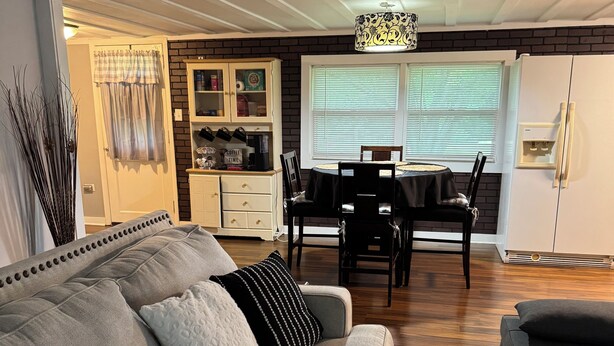 A living room with a grey sofa, a dining table, and a kitchen area with a fridge and cabinets.
