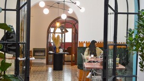 Ein Café mit einer Frau, die an einem Tisch sitzt, einer Vase mit Trockenpflanzen und einem gemusterten Fliesenboden.