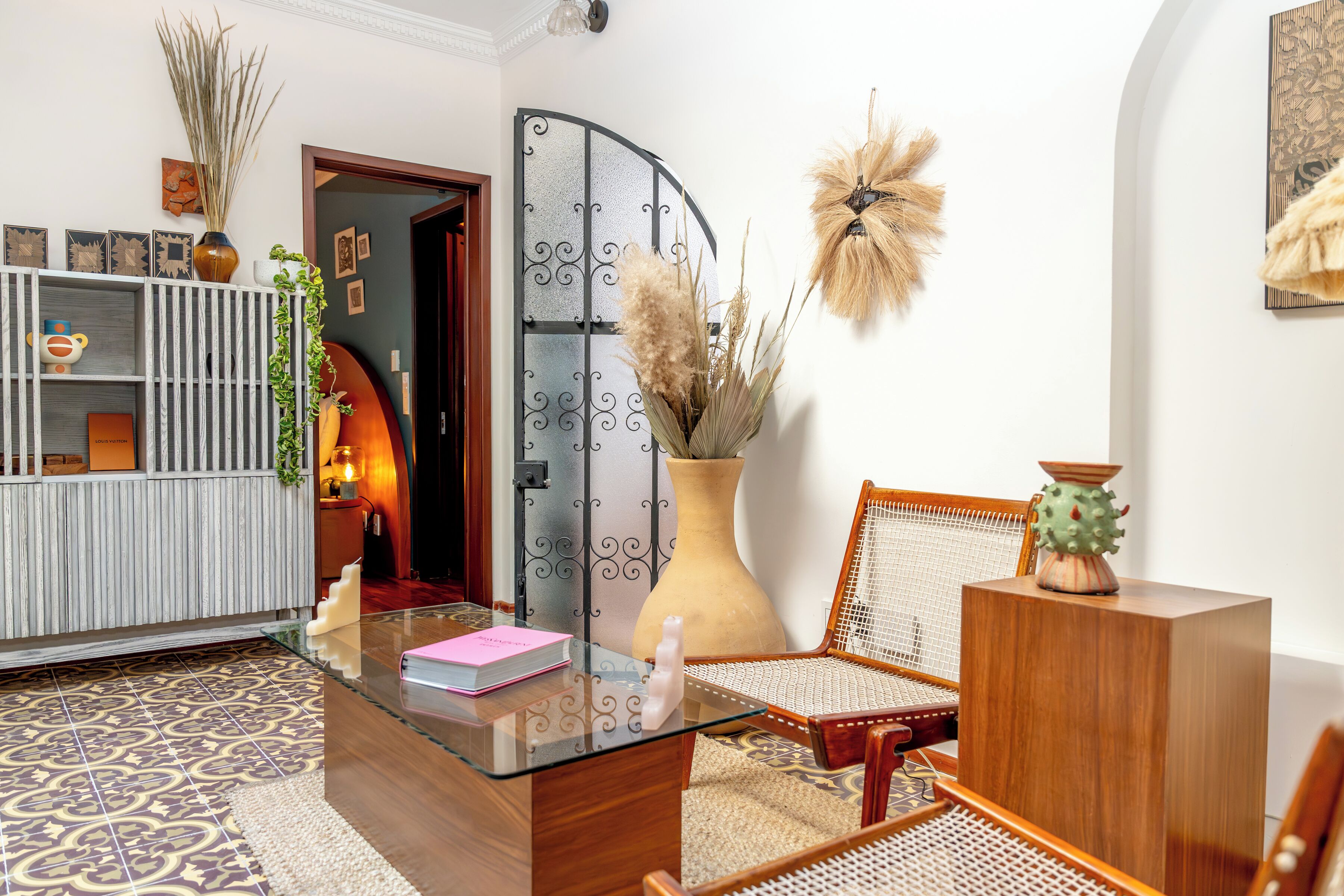 Una sala de estar moderna con una mesa de centro de vidrio, una silla de madera, una estantería y objetos decorativos.