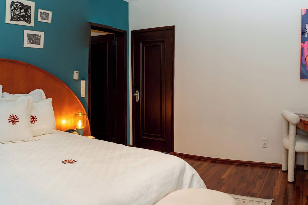 A bedroom with a large bed, bedside lamps, a desk with a chair, and artwork on the walls.