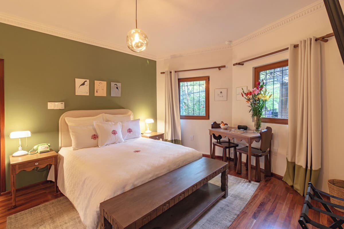 A bedroom with a large bed, bedside table, lamp, and a desk with a chair.