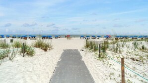 A beach pathway leading to beach umbrellas, a wooden boardwalk, and a sandy beach.