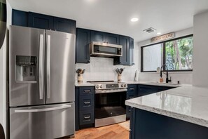 Une cuisine moderne dotée d’appareils électroménagers en acier inoxydable, de meubles de couleur bleu foncé et d’une grande fenêtre offrant une vue sur la verdure.