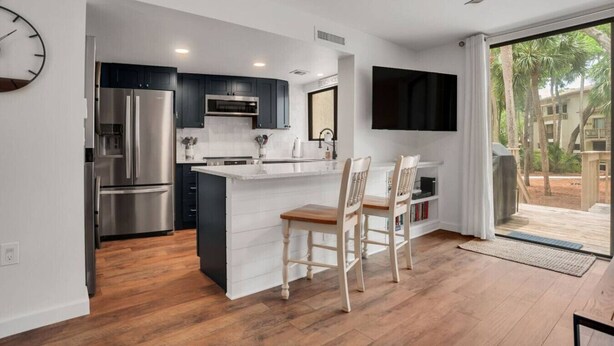 A modern kitchen with a central island, stainless steel appliances, and a dining area with two chairs.