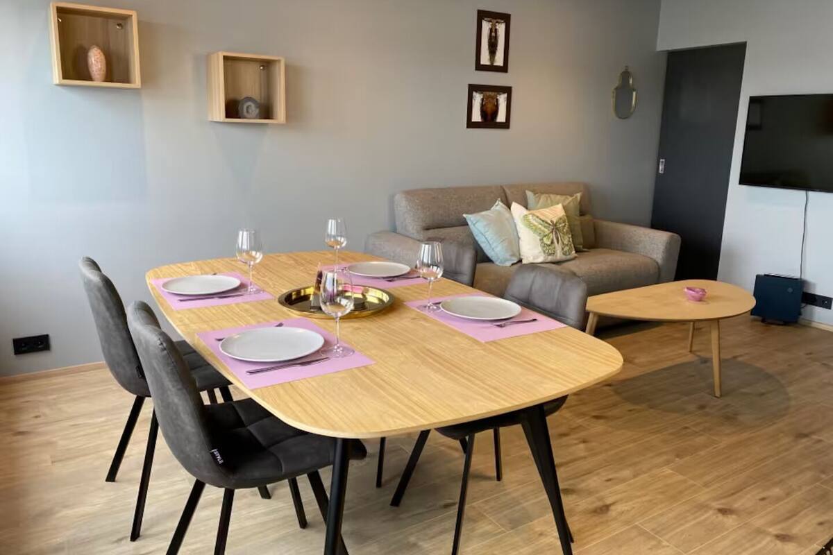 A dining area with a wooden table set for four, black chairs, and a grey sofa in the background.