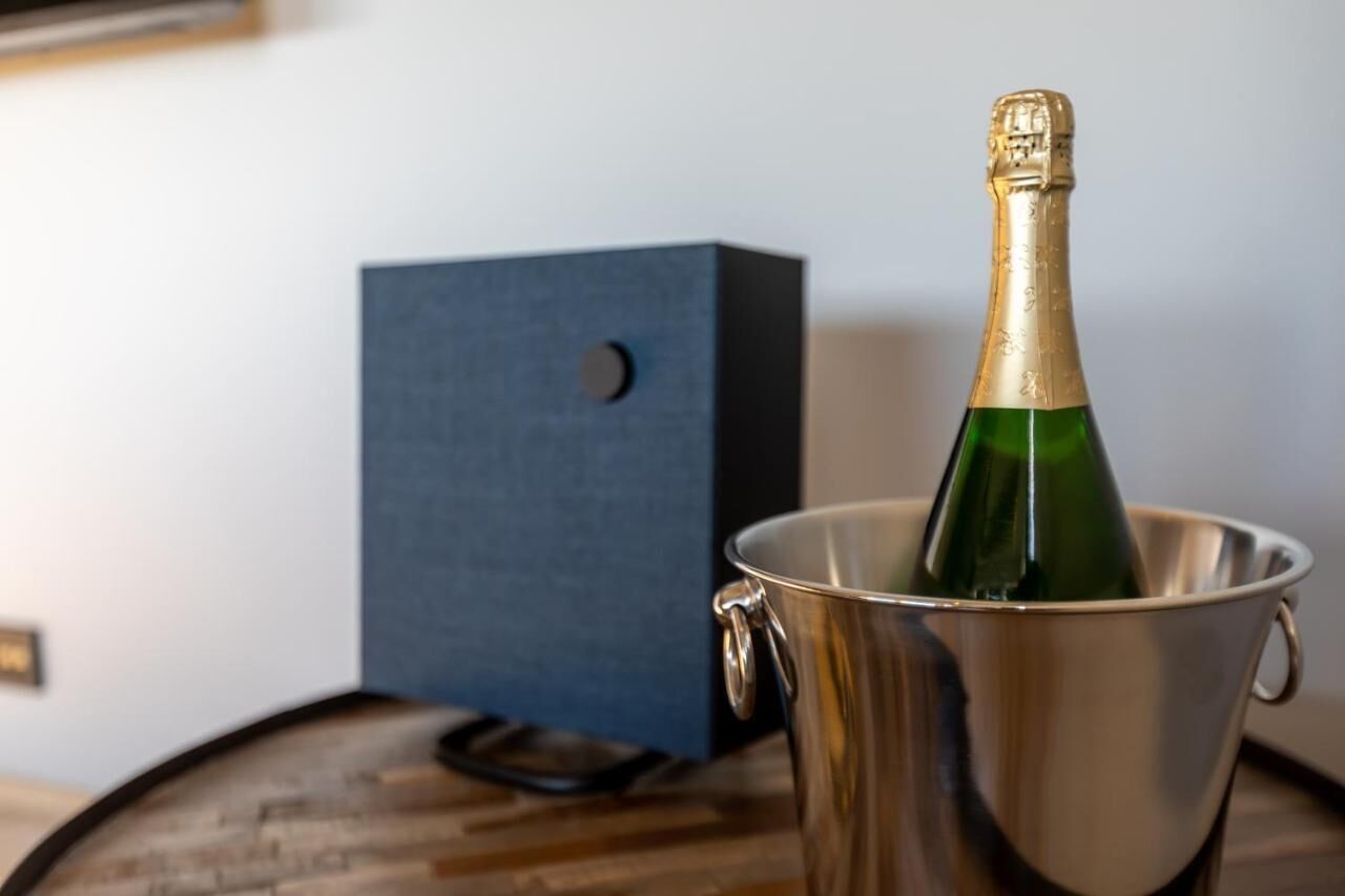 A bottle of champagne in a metallic bucket on a wooden surface with a dark blue box in the background.