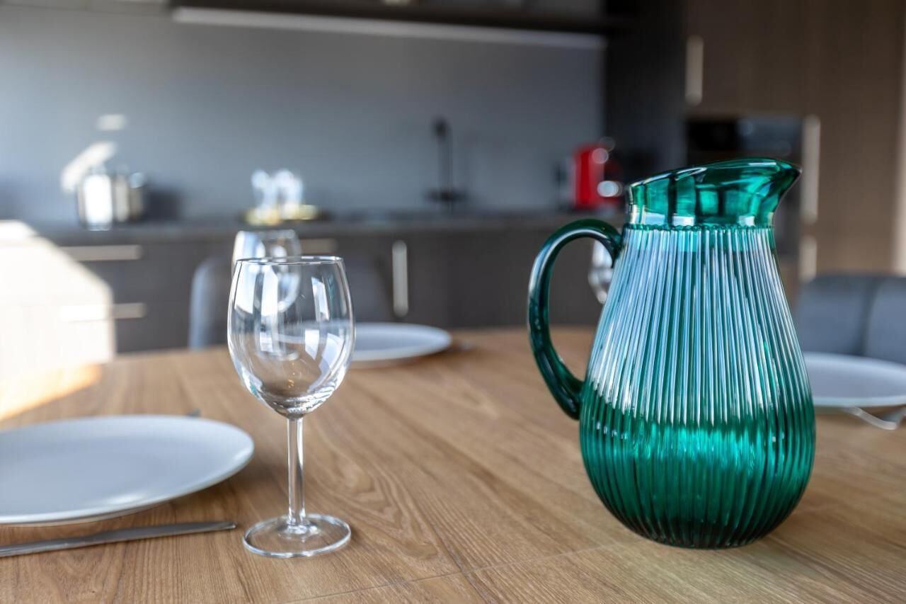A dining table with a clear glass wine glass and a green glass pitcher.