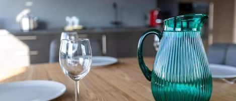 A dining table with a clear glass wine glass and a green glass pitcher.