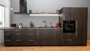 Una cucina moderna con pensili e basi in legno scuro, una cappa in acciaio inox, forno a incasso e una grande isola con lavello e diversi oggetti da cucina.