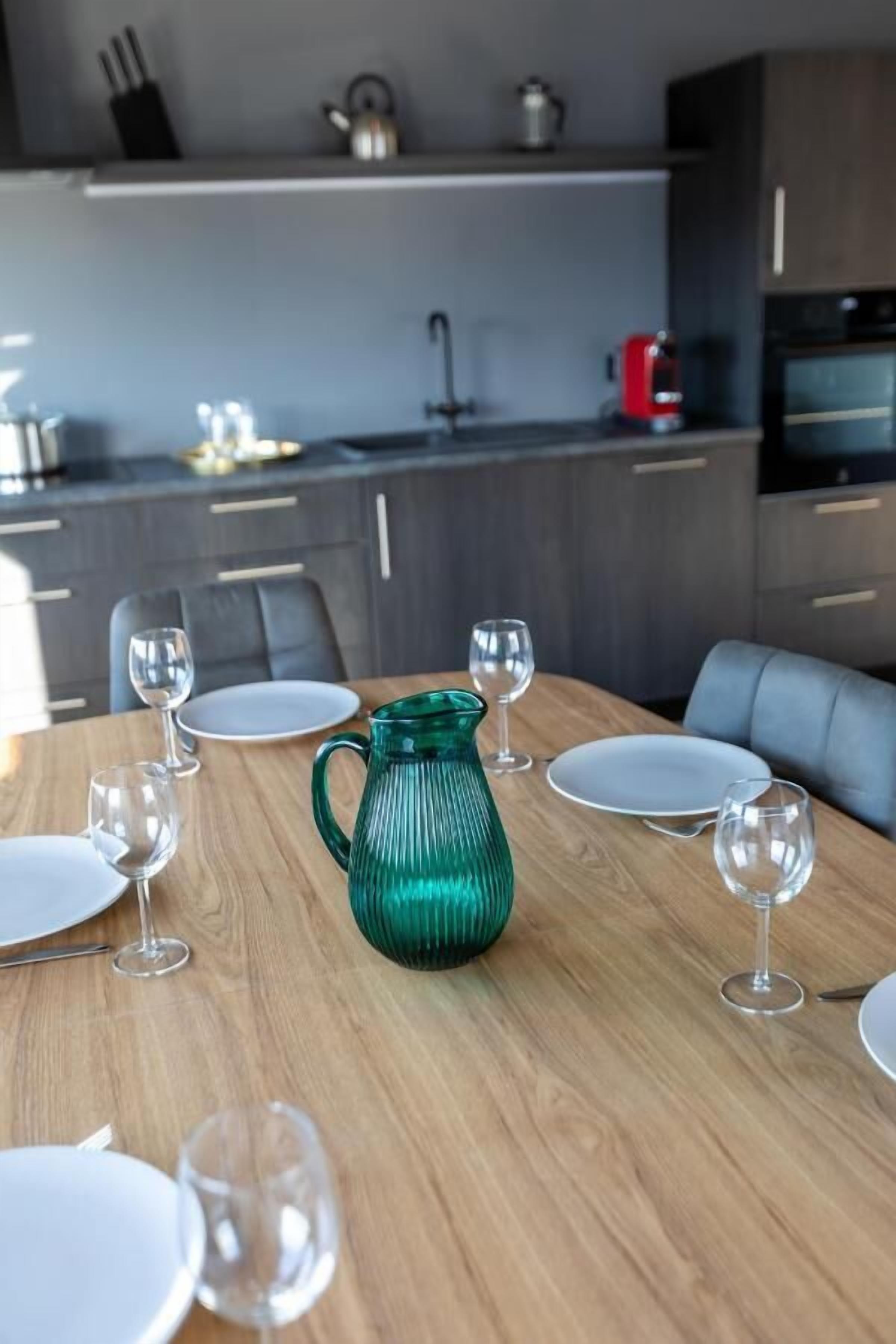 A modern dining area with a wooden table set for a meal, surrounded by grey upholstered chairs.