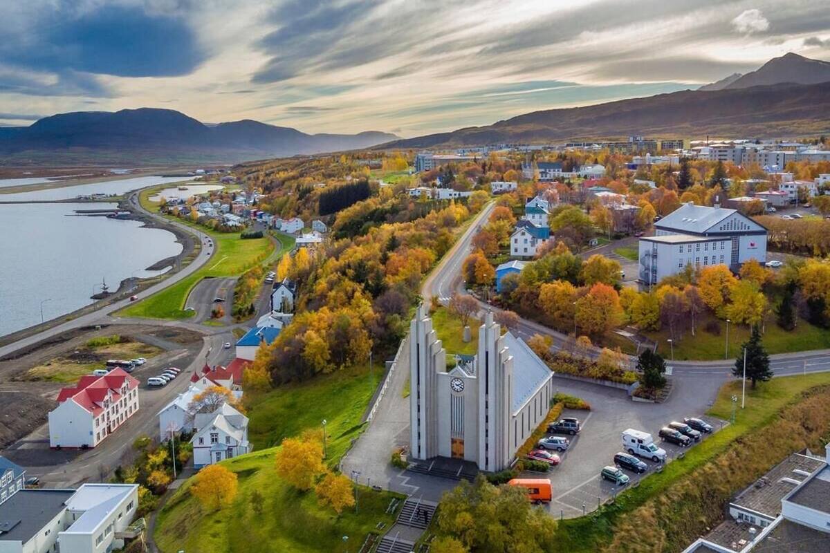 An aerial view of a town with a prominent church, a body of water, and autumn foliage.