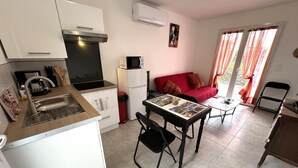A compact kitchen with a sink, stove, and microwave, a dining area with a table and chairs, a red sofa, and a window with curtains.