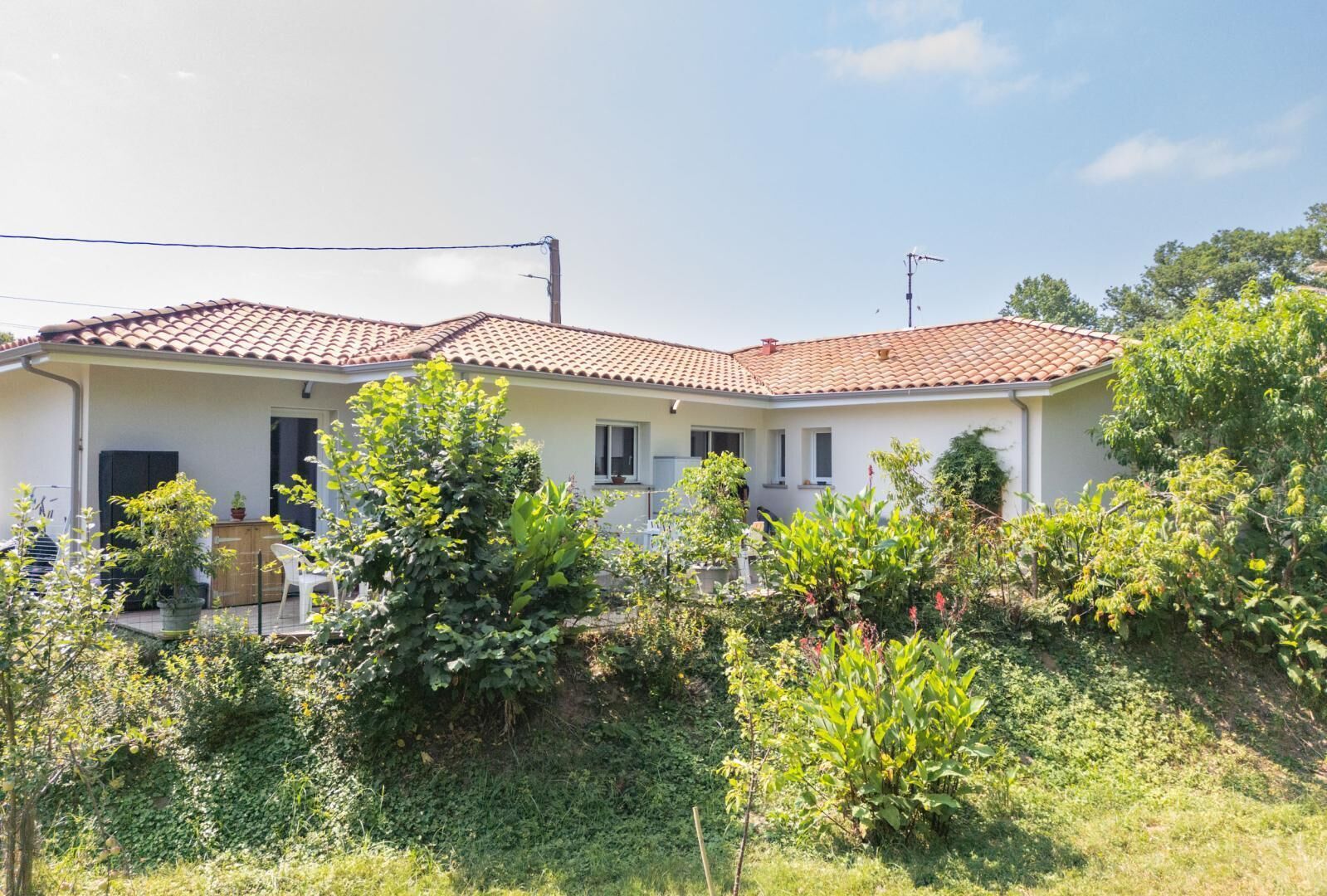 A two-story house with a tiled roof, a front porch, and a garden with various plants.