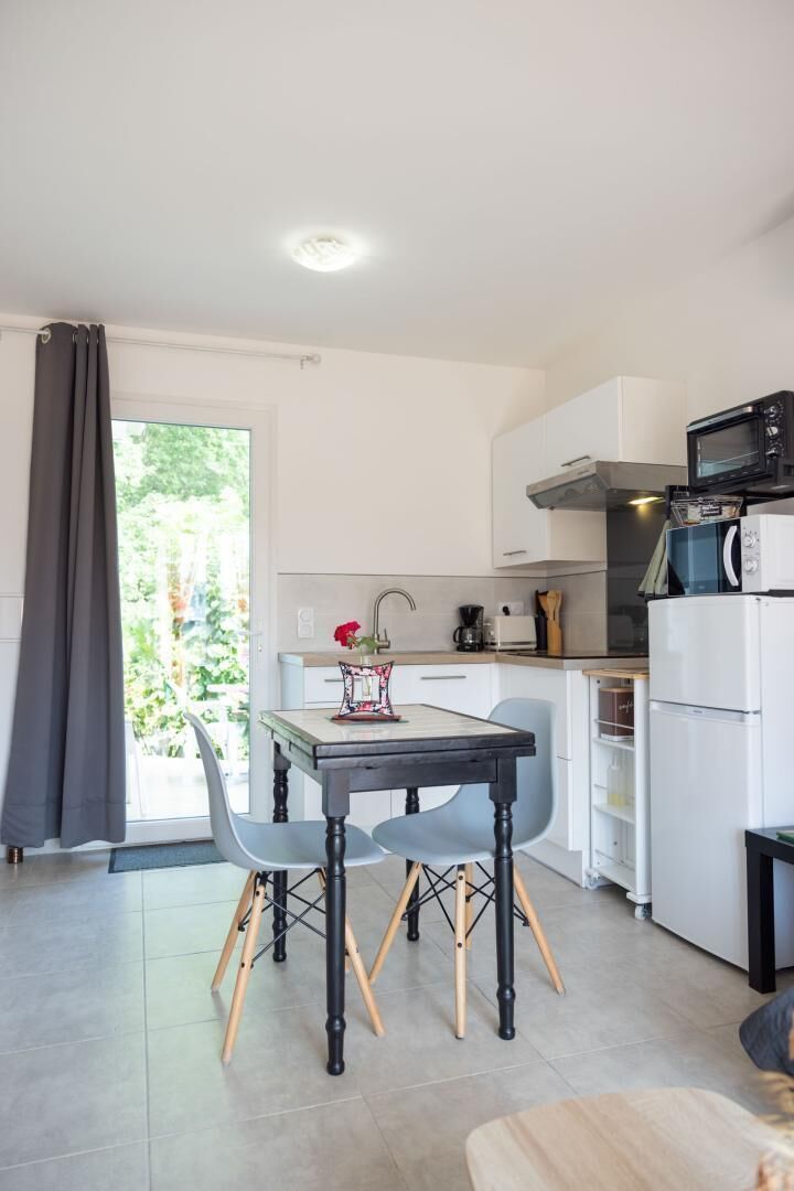 A compact kitchen with a dining area, a refrigerator, a microwave, and a window with curtains.