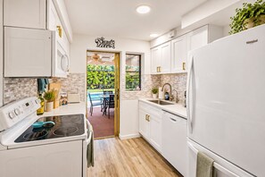 A modern kitchen with white cabinetry, a built-in oven, and a refrigerator. There is a window with a view of greenery outside.
