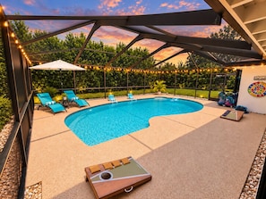 A swimming pool with lounge chairs and a deck area, surrounded by greenery and string lights.