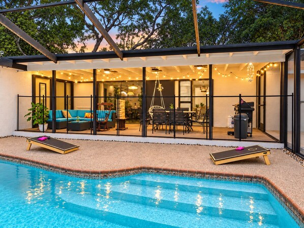 A modern outdoor pool area with a covered patio, seating, and a barbecue setup.