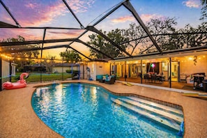 Une piscine entourée d’une structure en verre, avec des espaces de détente extérieurs et un patio couvert.