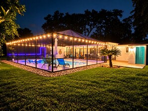 A covered outdoor swimming pool area with lounge chairs and string lights.