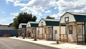 A row of small, single-story cabins with green roofs, wooden railings, and a clear sky. - Tiny Oasis #1 - Hurricane, UT (Hurricane)
