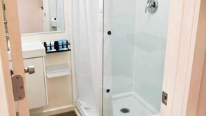 A modern bathroom with a glass shower enclosure, a toilet, and a vanity with toiletries. - Tiny Oasis #1 - Hurricane, UT (Hurricane)