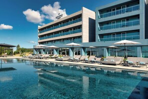 A modern hotel with a clear pool, sun loungers, and umbrellas.