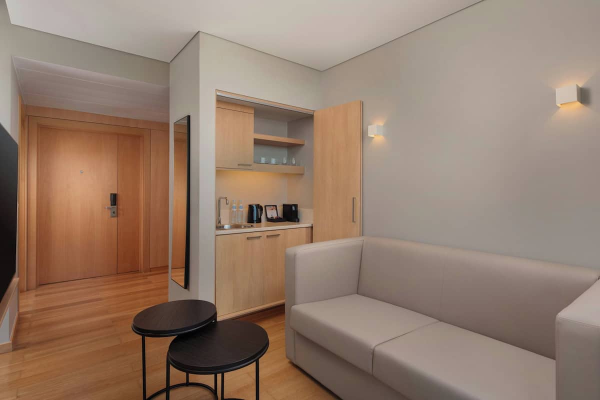 A modern room with a sofa, a small table, a kitchen area with cabinets and a countertop, and a door leading to another room.