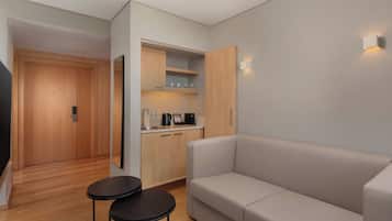 Une pièce moderne comprenant un canapé, une petite table, un coin cuisine avec des placards et un plan de travail, ainsi qu’une porte donnant sur une autre pièce.