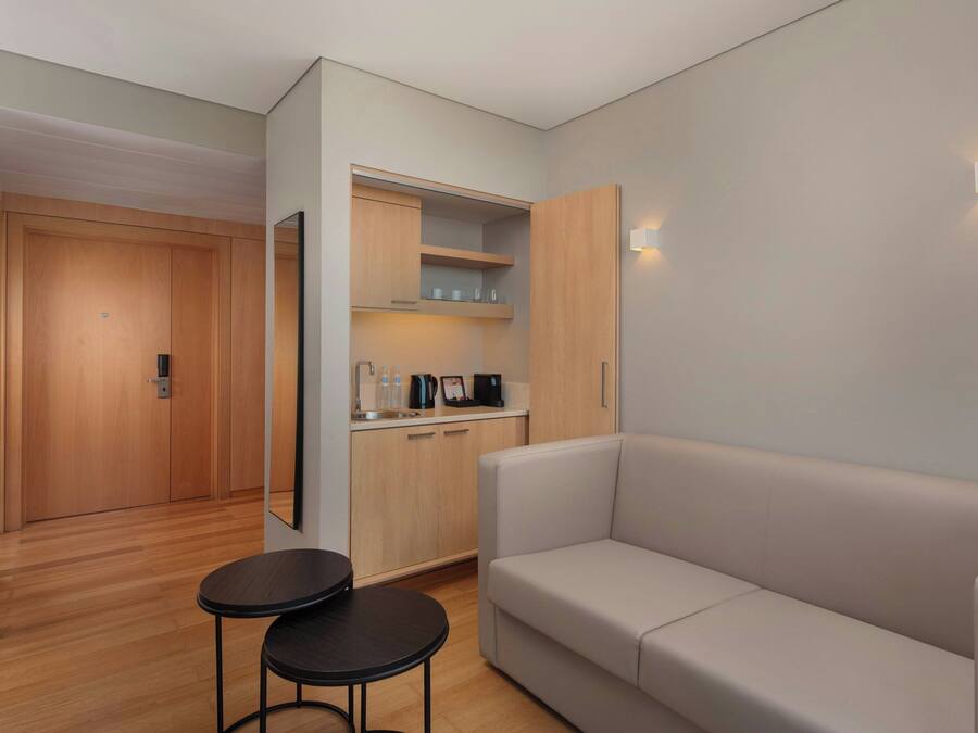 Una habitación moderna con sofá, una mesita, una zona de cocina con armarios y encimera, y una puerta que da a otra habitación.