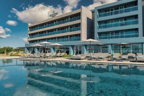 A modern hotel with a pool area, multiple floors, and a clear sky.