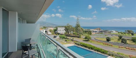 A balcony with a pool, chairs, and a view of the ocean and surrounding landscape.