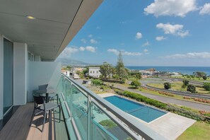 A balcony with a pool, chairs, and a view of the ocean and surrounding landscape.