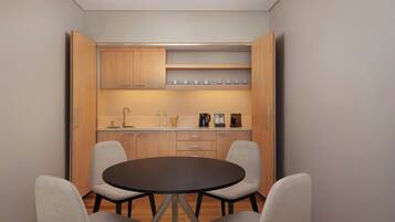 Cozinha compacta com mesa redonda para refeições e quatro cadeiras, armários de madeira e bancada com diversos eletrodomésticos e utensílios.