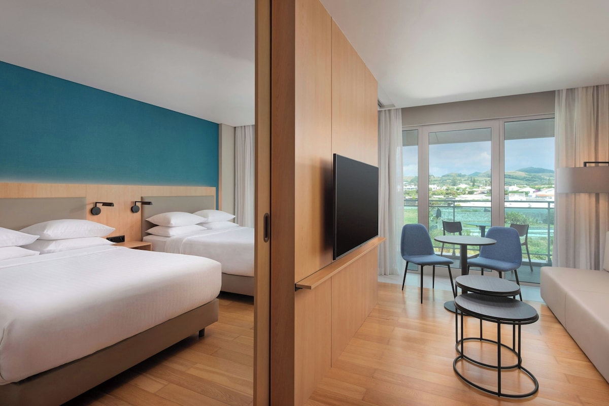 Una habitación de hotel con dos camas, televisión, una mesita con sillas y un sofá.