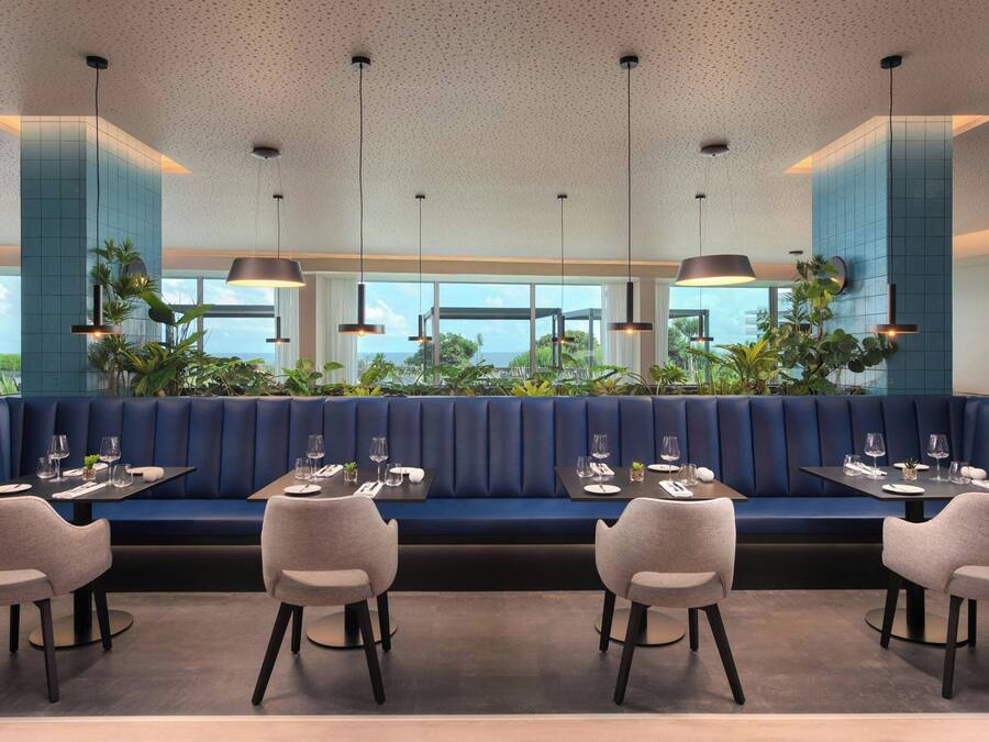A modern restaurant with a blue booth seating area, multiple tables with chairs, and hanging pendant lights.