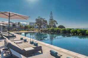 A poolside area with lounge chairs and umbrellas, a clear blue sky, and a view of a white building and trees. - Delta Hotels by Marriott Azores (Ponta Delgada)